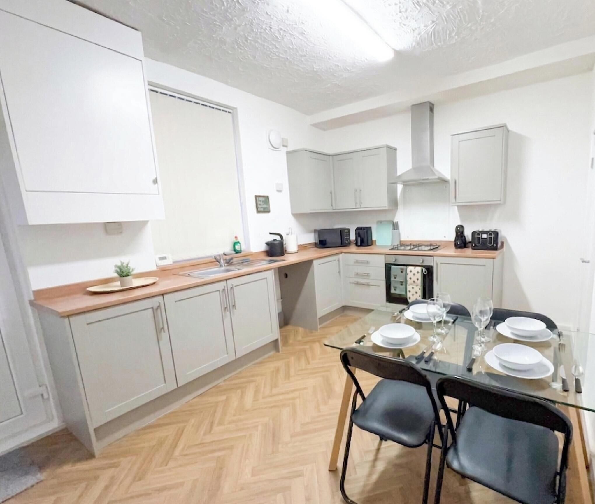 A compact kitchen with white cabinets, a herringbone floor, a dining table with chairs, and a microwave.