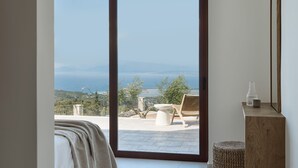 Ein Zimmer mit einer großen Schiebeglaswand, die auf eine Terrasse mit Blick auf das Meer und die Hügel führt.