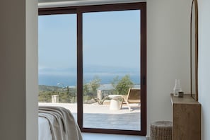 A room with a large sliding glass door leading to an outdoor terrace with a view of the sea and hills. - Anemones Villas (Lefkada)