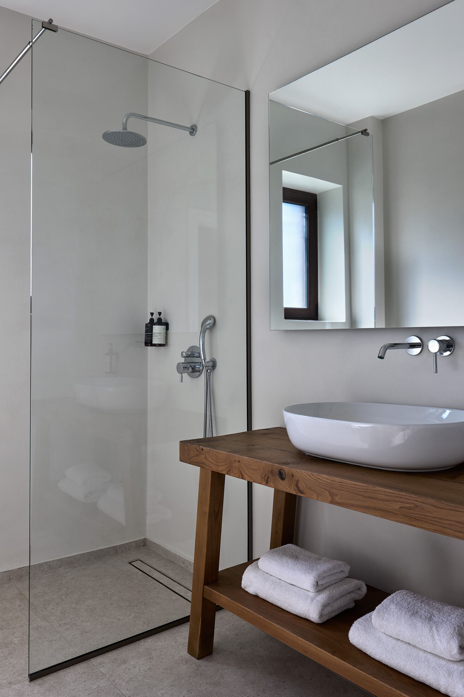 A modern bathroom with a glass shower enclosure, a wooden vanity with a white sink, and a mirror above the sink.