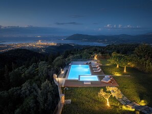 Una piscina con sillas de descanso y vistas a la ciudad al anochecer.