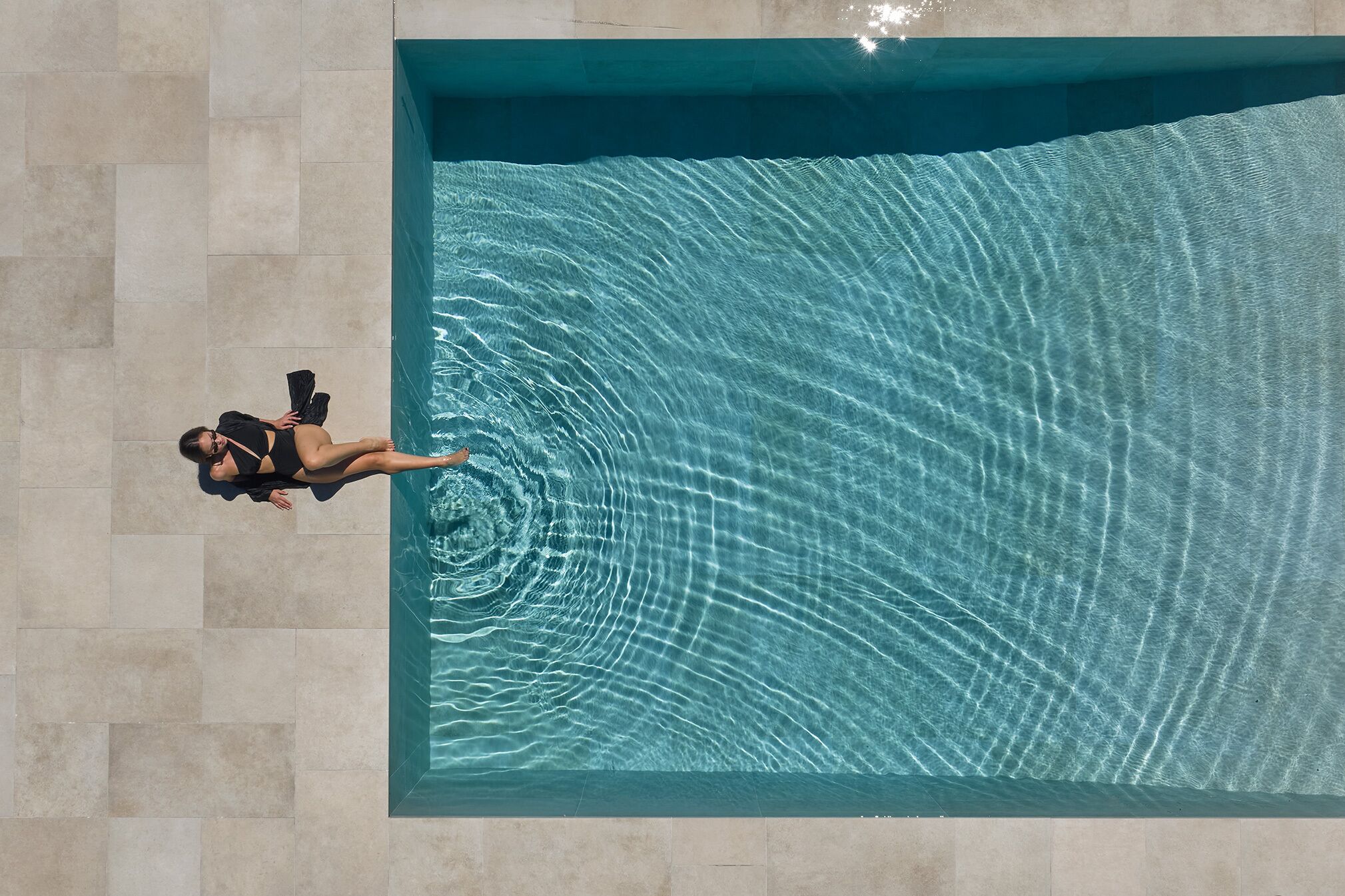 A person in a black swimsuit standing in a rectangular pool with clear water.