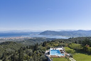 A pool with lounge chairs, a view of a coastal town, and a mountainous landscape. - Anemones Villas (Lefkada)