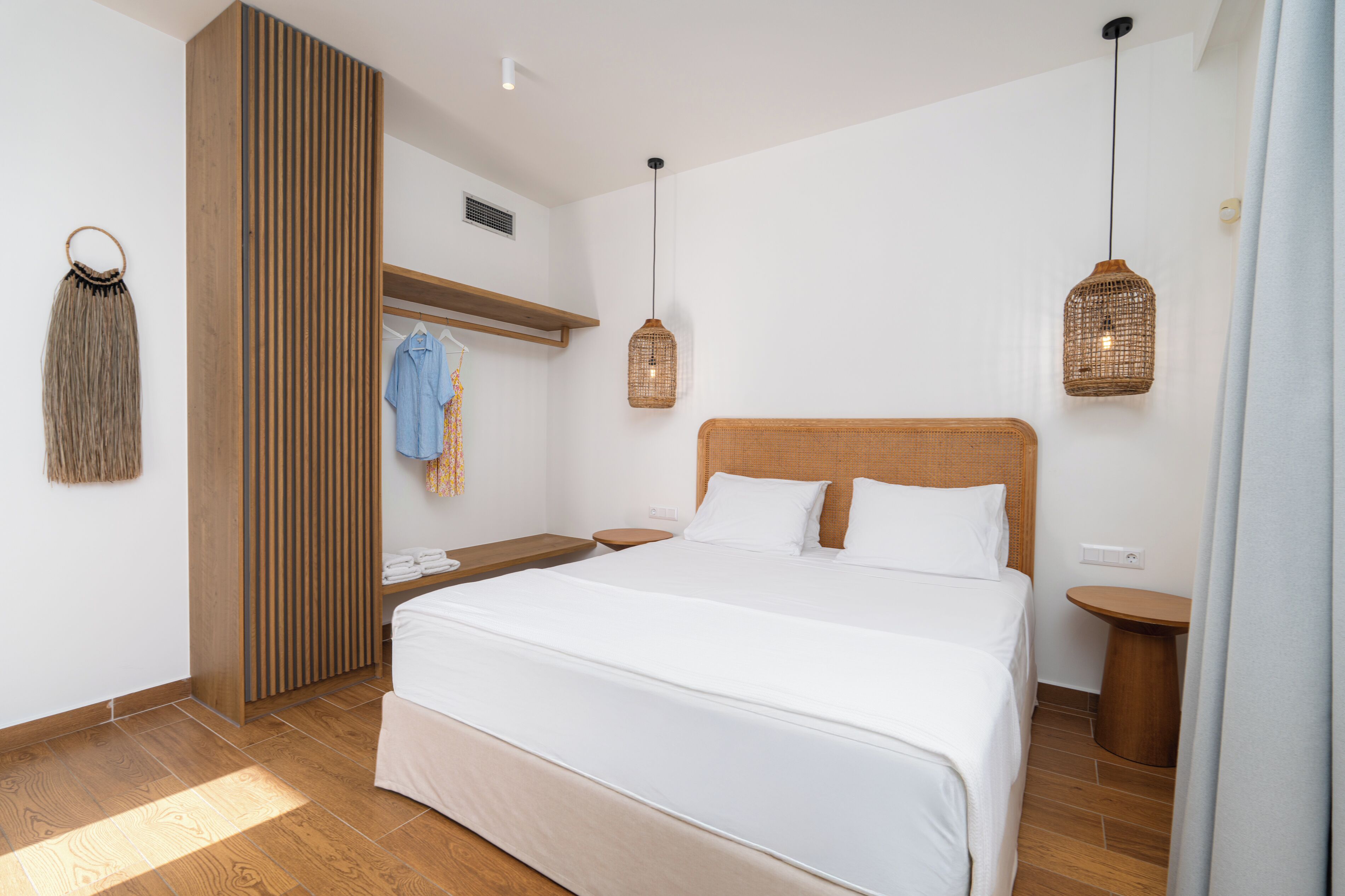 A bedroom with a large bed, wooden headboard, two bedside tables, a hanging light fixture, and a wardrobe.
