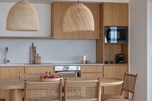 A modern kitchen with wooden cabinets, a built-in microwave, and a dining area with wicker chairs and a table. - Anemones Villas (Lefkada)