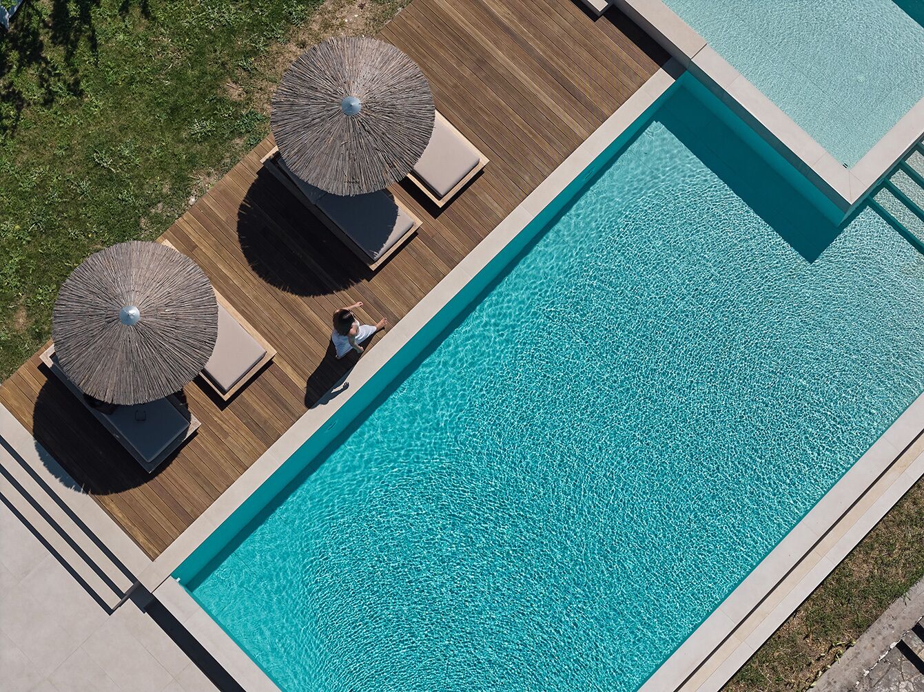 En rektangulär swimmingpool med två solstolar och parasoller på ett trädäck.