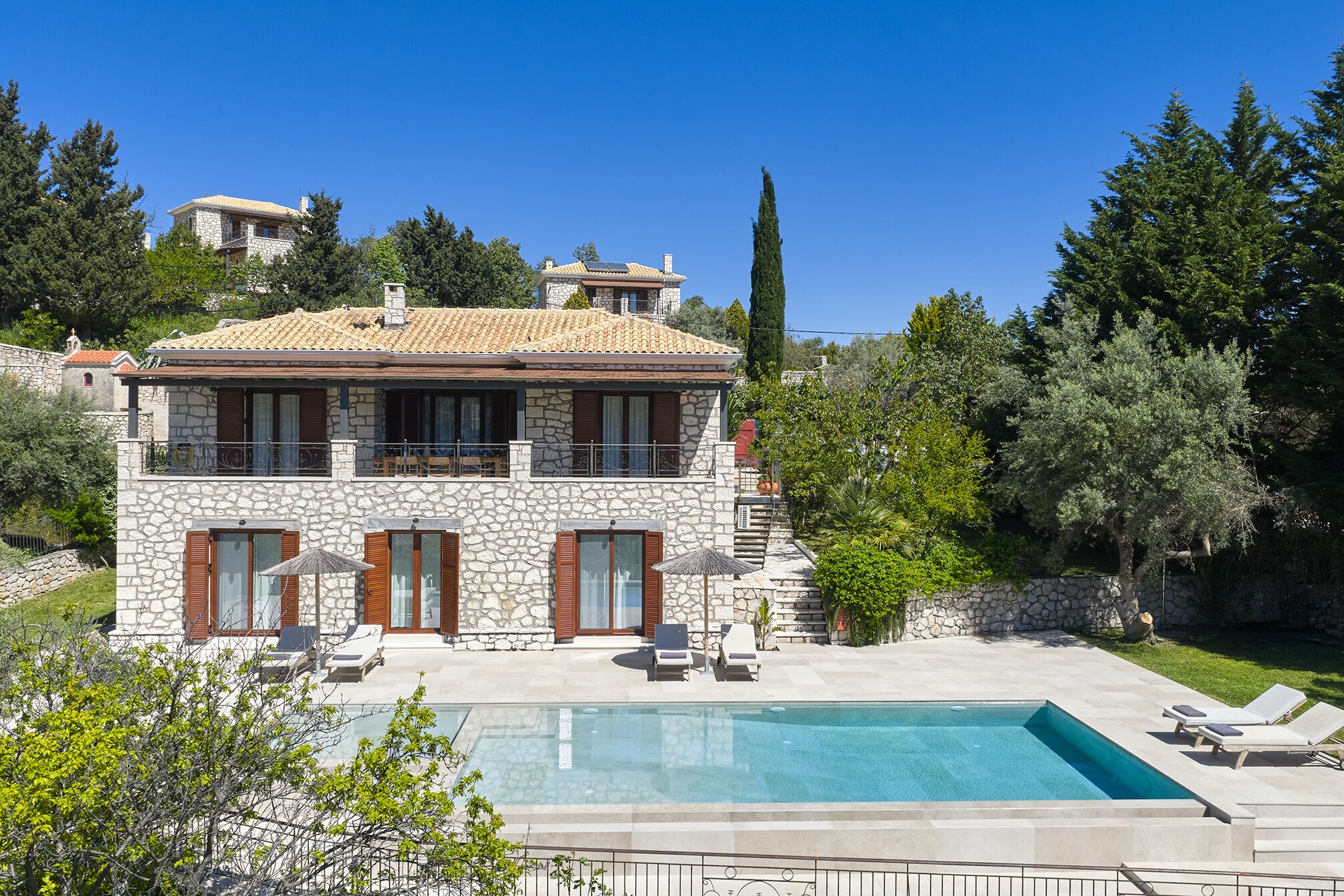 A two-story stone house with a swimming pool and lounge chairs.