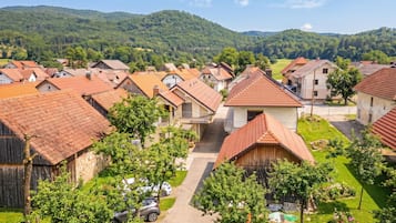 A residential area with houses having red-tiled roofs, surrounded by greenery and hills.