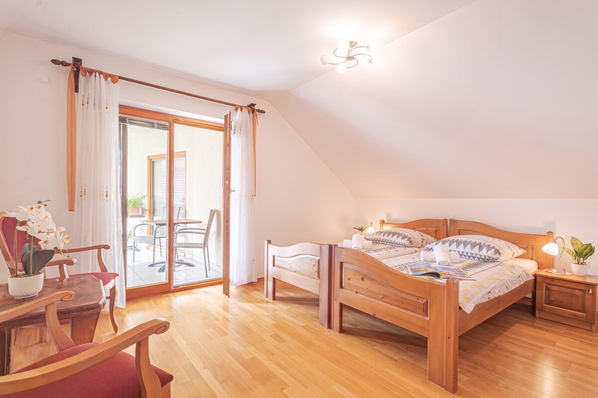 Een slaapkamer met een houten bed, een nachtkastje, een bureau met een stoel en een schuifdeur naar een buitenruimte.