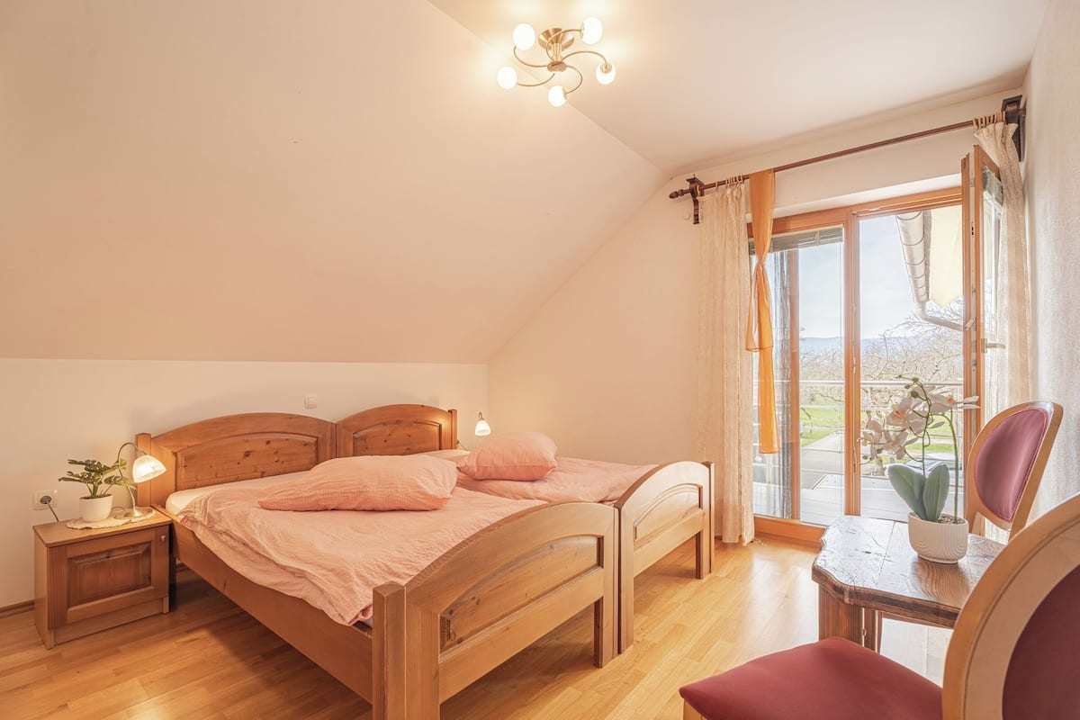 Un dormitorio con una cama de madera, una mesita de noche con una lámpara, una silla y vistas a través de un ventanal grande.