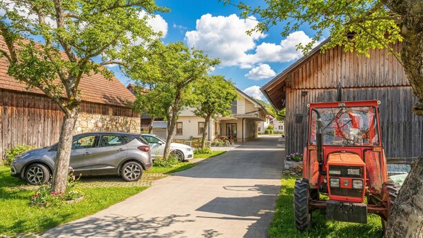Une rue de campagne avec une voiture garée, un tracteur et des bâtiments en bois.