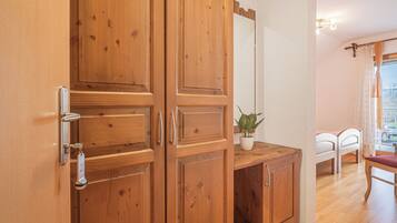 A wooden wardrobe with a mirror, a small potted plant, and a bed with white bedding in the background.