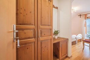 Un armario de madera con espejo, una pequeña planta en maceta y una cama con ropa de cama blanca al fondo.