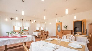 Un espace repas avec des tables disposées pour accueillir quatre personnes, des chaises en bois, un éclairage suspendu et une vue sur la salle à manger.