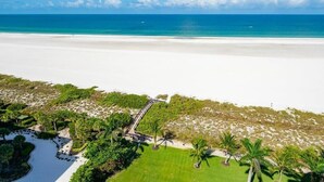 Un complexe hôtelier de bord de mer doté d’une plage de sable blanc, d’un océan d’un bleu limpide et d’un sentier menant à un bâtiment.