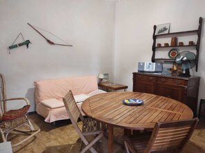 A cozy room with a wooden dining table, a rocking chair, a sofa, and a cabinet with a fan. - Villa near the beach with garden, private parking for families,groups & climbers (san vito lo capo)