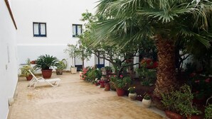 Ein Innenhof mit Fliesenboden, Blumentöpfen, einem weißen Liegestuhl und einem Gebäude mit Fenstern.