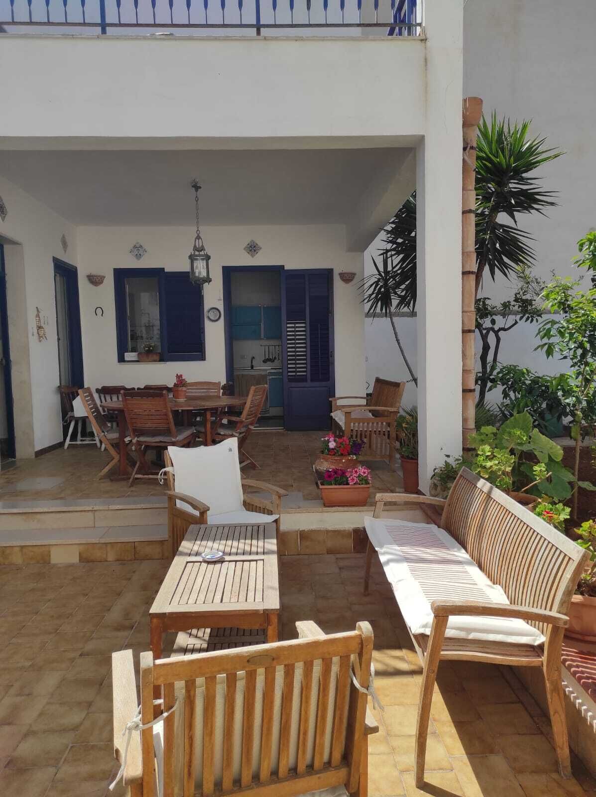 Eine überdachte Terrasse im Freien mit Holzmöbeln, einem Esstisch und Topfpflanzen.