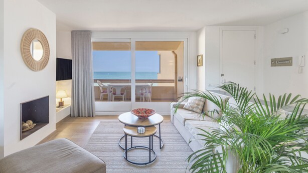 Ein Zimmer mit Sofa, Tisch mit Schale, Fernseher, Kamin, Pflanze und Meerblick durch eine Glastür.