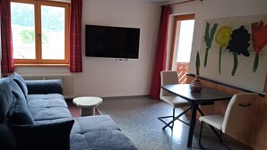 Huoneessa on sohva, pieni pyöreä pöytä, seinälle asennettu televisio ja seinällä oleva taulu.