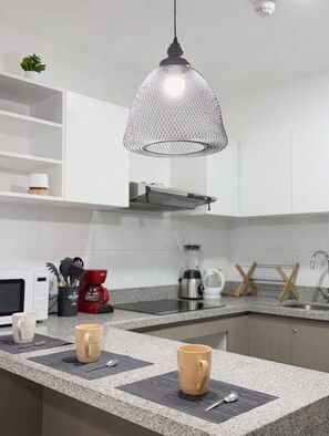 A kitchen with a granite countertop, a coffee maker, a microwave, and a hanging pendant light. - Apartment in Downtown Cusco / 4–5 People / High-Speed Wi-Fi (Cusco)