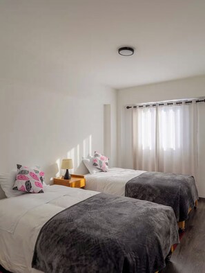 Habitación de hotel con dos camas, una mesita de noche, una lámpara y una ventana con cortinas.