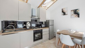 A modern kitchen with a skylight, a dining area with a wooden table and chairs, and abstract wall art. - Hilten Luxury Sunset Holiday Home with Mountain View, Private Garden and Wi-Fi (Isola delle Femmine)