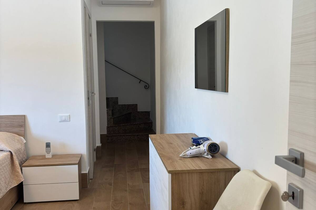A narrow hallway with a bed, a desk, a chair, and a mirror on the wall.