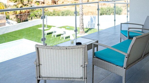 A balcony with wicker furniture and a view of a landscaped area.