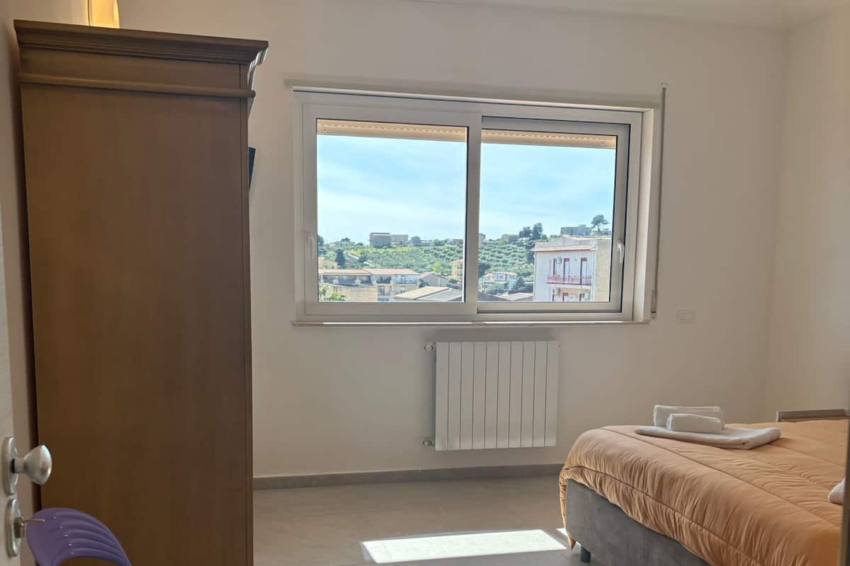 A bedroom with a bed, a window, a radiator, a chair, and a wardrobe.