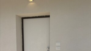 A door with a light switch and a keyhole, a small recessed light above it, and a corner with a white baseboard.