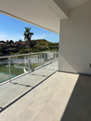 Balcón con vista despejada a una piscina, una palmera y edificios distantes.