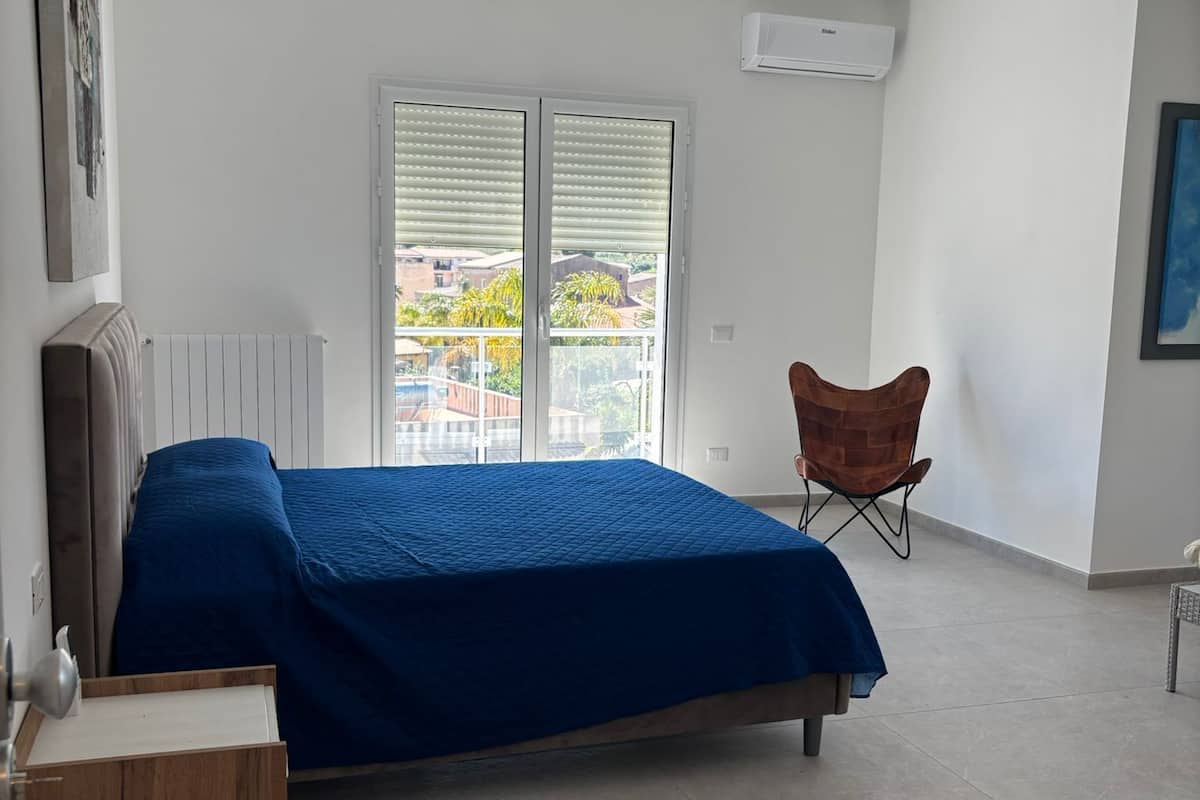 A bedroom with a bed, a chair, a radiator, and a window with blinds.