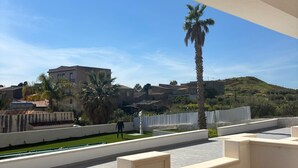 A modern room with a view of a green lawn, a palm tree, and buildings in the distance.