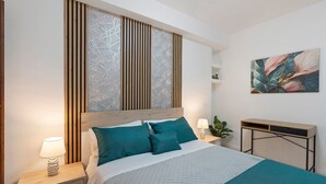 Een keurig opgemaakt slaapkamer met een bed, nachtkastjes, een bureau en een kunstwerk aan de muur.