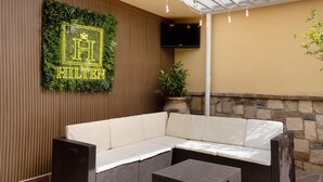 Een overdekt terras met een bank en een tafel, een aan de muur bevestigde televisie en een bord met een logo.