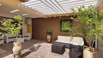 Un patio cubierto con mobiliario exterior, plantas en macetas y un muro decorativo.