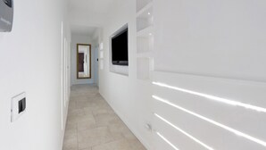 Een gang met witte wanden, inbouwverlichting, een flatscreen televisie aan de wand en een deur aan het einde.