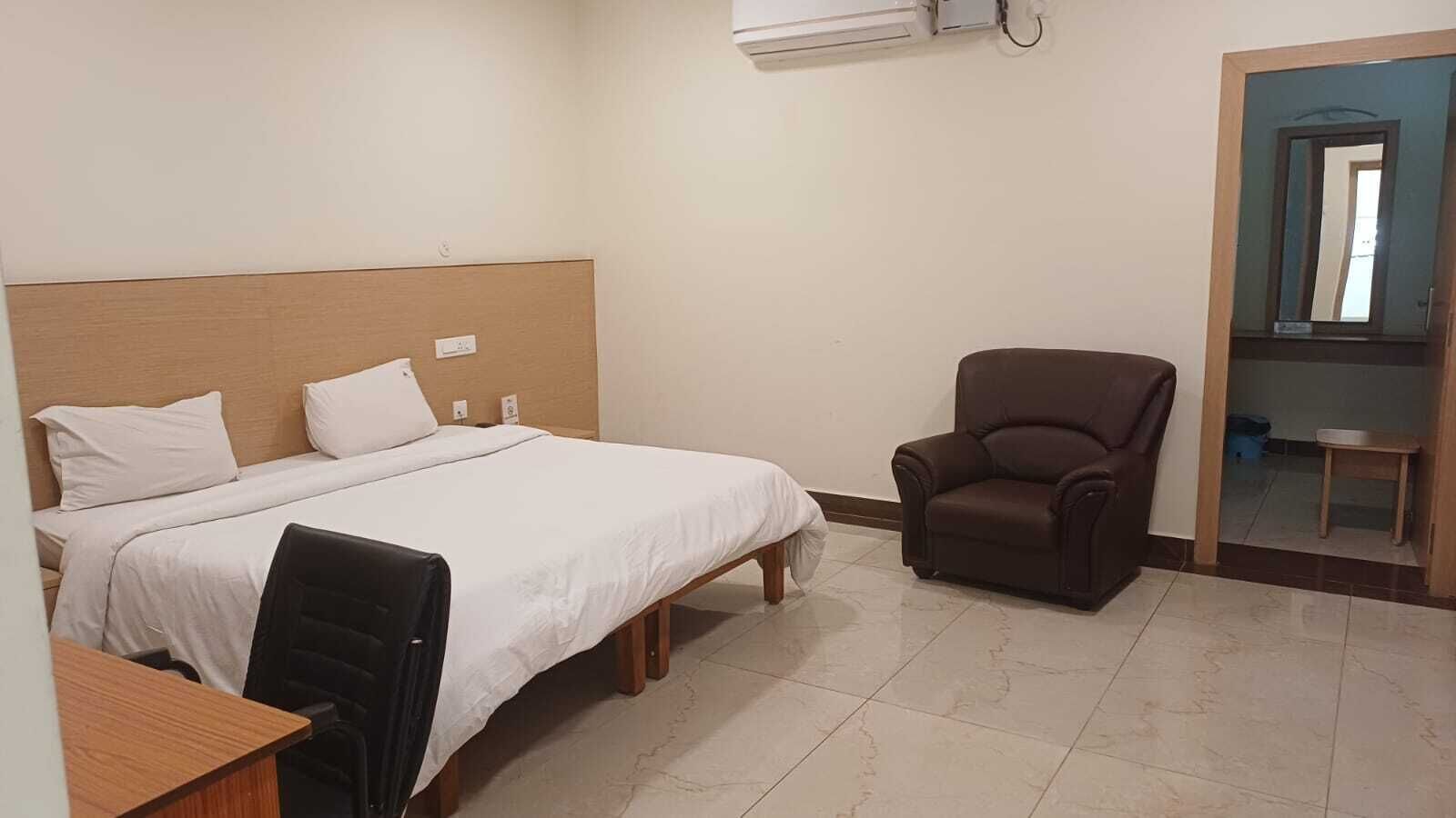 A hotel room with a bed, a desk, a chair, and a mirror.