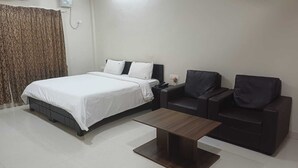 A hotel room with a bed, two dark sofas, a small table, and a curtain. - Hotel Tamilnadu Trichy (Tiruchirappalli)
