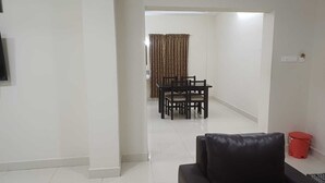 A living room with a black sofa, a dining table with chairs, a red trash bin, and a patterned curtain in the background. - Hotel Tamilnadu Trichy (Tiruchirappalli)