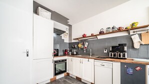 Una cucina moderna con mobili bianchi, lavastoviglie, macchina del caffè e bollitore sul piano di lavoro.