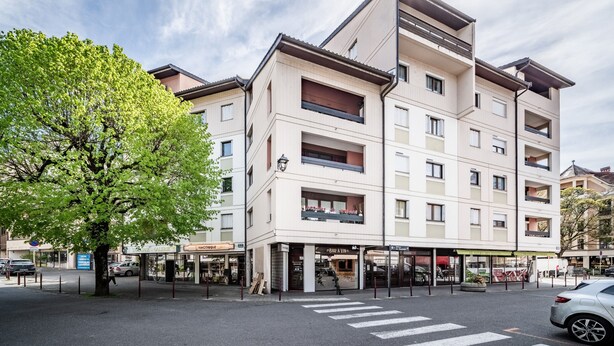 Un edificio a più piani con un negozio al piano terra, un attraversamento pedonale e un albero.