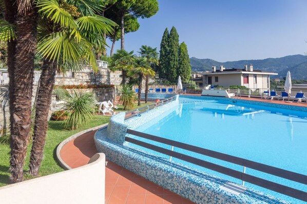Une piscine dont le bord est recouvert de carreaux, entourée de palmiers et d’un mur de pierre.
