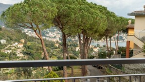 A balcony with a view of a coastal town, trees, and a road. - CASA CONCETTA - View with a balcony and a large window (Rapallo)