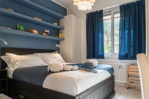 Une chambre à coucher comprenant un lit, une table de chevet, une chaise, une fenêtre avec des rideaux et une étagère intégrée remplie de livres.