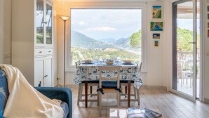 A dining area with a table set for two, a sofa, and a view of a mountainous landscape through a large window. - CASA CONCETTA - View with a balcony and a large window (Rapallo)