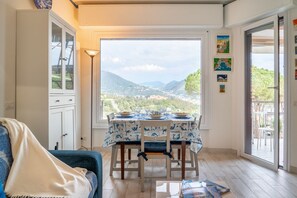 Un coin repas avec une table dressée pour deux personnes, un canapé et une vue sur un paysage montagneux par le biais d’une grande fenêtre.