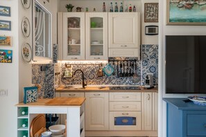 Une cuisine avec des meubles blancs, un pare-feu en carrelage et un plan de travail en bois.