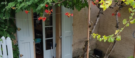 Un bâtiment rustique, doté d’une clôture en bois, d’une pergola couverte de vigne et d’une porte avec des volets.